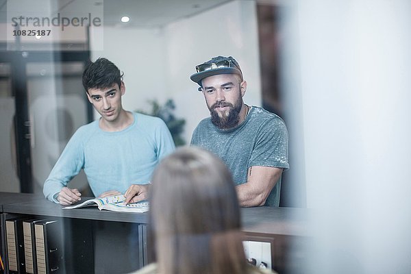 Zwei junge Männer  die die Rezeptionistin im Büro befragen.