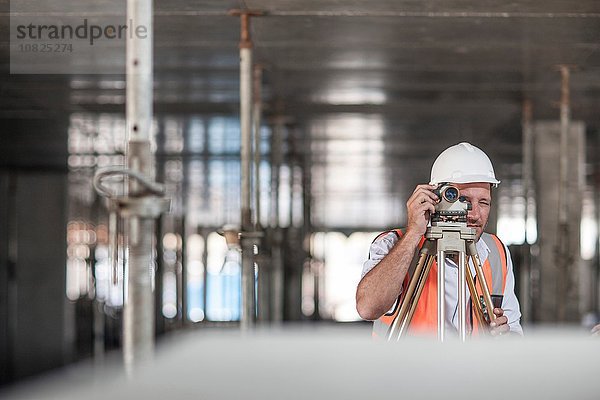 Mittlerer erwachsener Landvermesser mit Theodolit auf der Baustelle