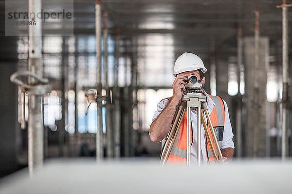 Mittlerer erwachsener Landvermesser  der auf der Baustelle durch Theodolit schaut