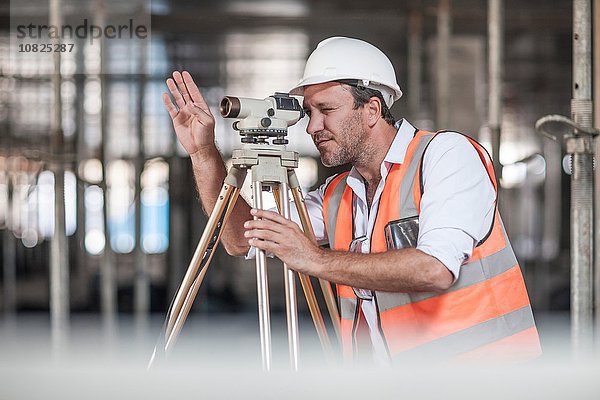 Vermessungsingenieur beim Durchschauen von Theodolit auf der Baustelle