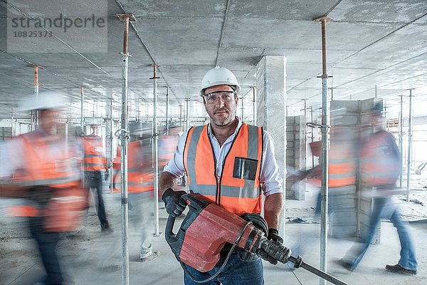 Mittlerer erwachsener Baumeister mit Baumaschinen auf belebter Baustelle