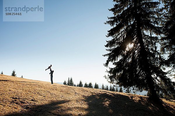 Silhouette eines Mannes  der die Tochter eines Kleinkindes auf dem Hügel hält  Tegernsee  Bayern  Deutschland