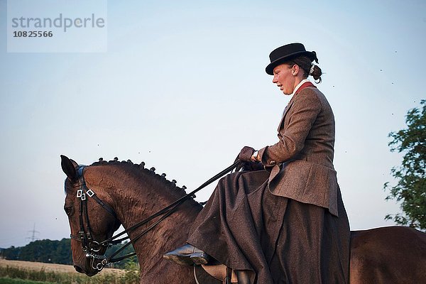 Mittlere erwachsene Frau reitet und trainiert Dressurpferd im Gelände