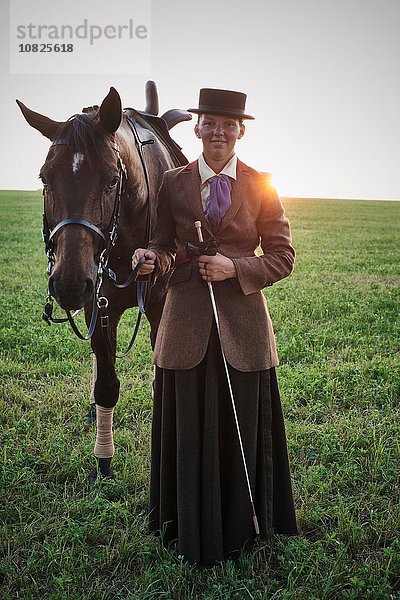 Porträt einer stehenden Frau mit Dressurpferd im Feld