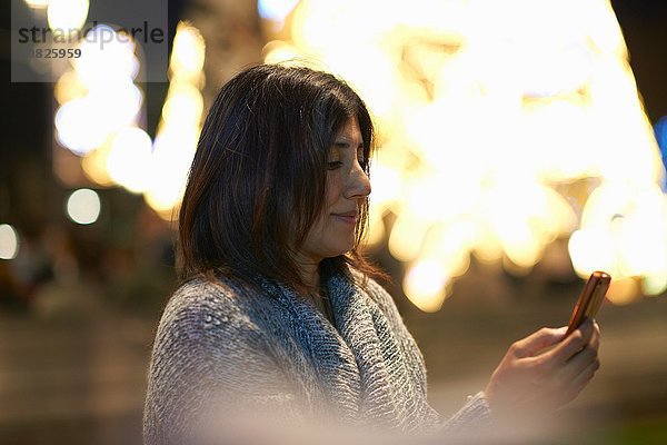 Frau mit Smartphone  dekorative Beleuchtung im Hintergrund
