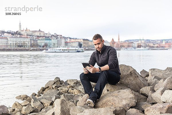 Junger Mann auf Felsen sitzend mit digitalem Tablett  Budapest  Ungarn