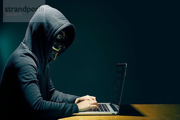 Seitenansicht der Person mit Kapuze und Guy Fawkes Gesichtsmaske mit Laptop