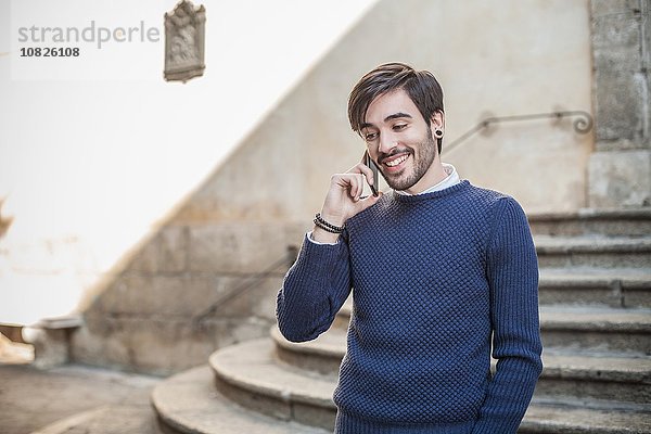 Junger Mann vor Steintreppe mit Smartphone lächelnd