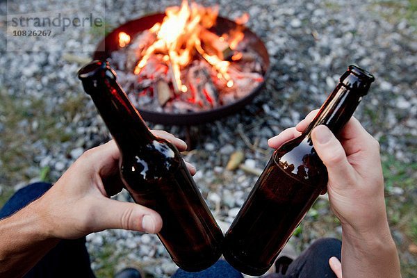 Hände halten Bierflaschen mit Lagerfeuer