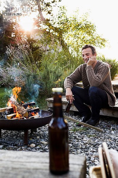 Reifer Mann am Feuer mit Bier sitzend  entspannend