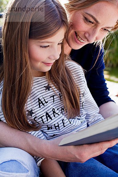 Mutter und Tochter lesen gemeinsam ein Buch  lächelnd