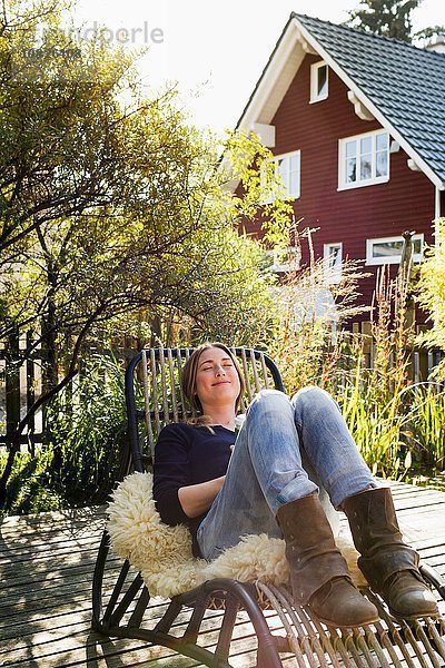 Mittlere erwachsene Frau entspannt sich auf einem Liegestuhl auf einer Holzterrasse.
