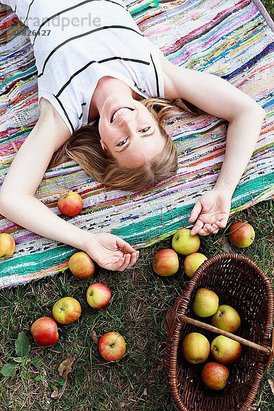 Frau auf gestreiftem Teppich liegend mit Apfelkorb