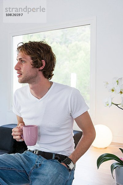 Junger Mann im Wohnzimmer beim Kaffeetrinken