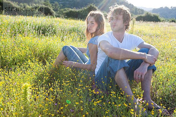 Romantisches junges Paar  Rücken an Rücken im Wildblumenfeld  Mallorca  Spanien