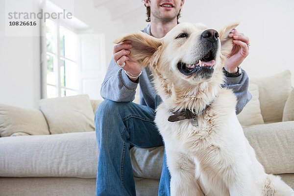 Junger Mann auf dem Wohnzimmersofa mit Ohren von Golden Retriever Dog