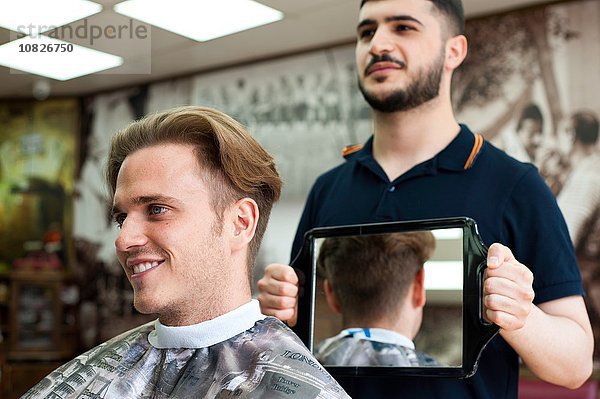 Friseur mit Spiegel für lächelnden Kundenhaarschnitt