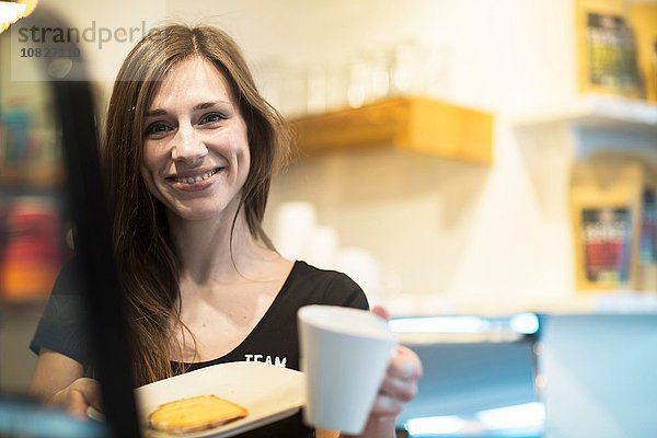 Porträt einer jungen Kellnerin mit Kaffee und Kuchen im Café