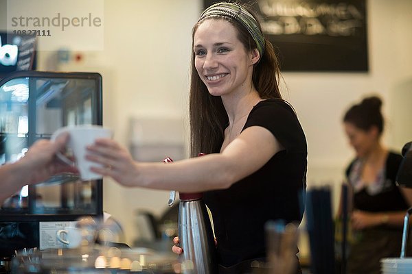 Junge Kellnerin überreicht Kaffee an Café-Kundin