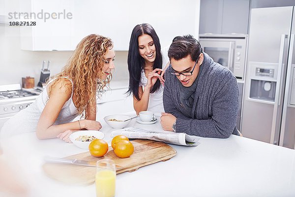 Drei junge Erwachsene lesen Zeitung am Küchentisch