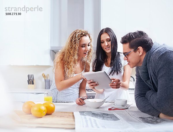 Drei junge Erwachsene mit digitalem Tablett an der Küchenzeile