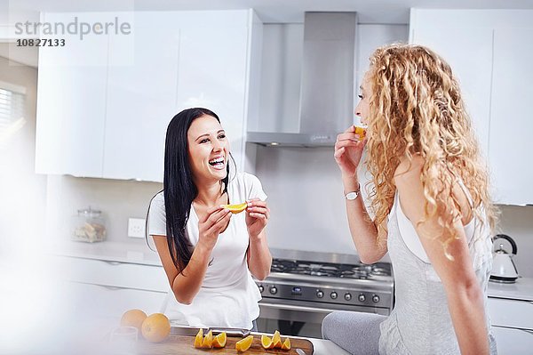 Zwei junge Freundinnen beim Frühstücken von Orangen am Küchentisch