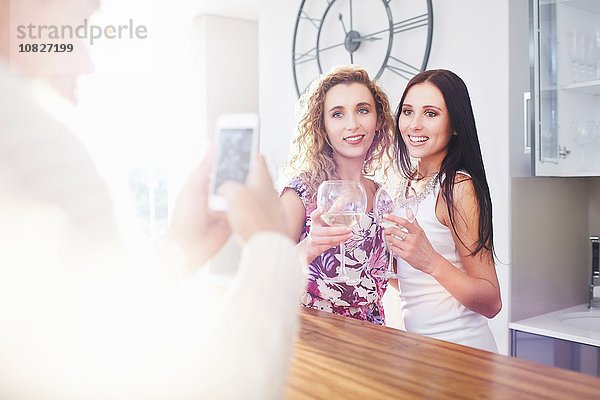 Junger Mann fotografiert weibliche Freunde auf dem Smartphone in der Küche