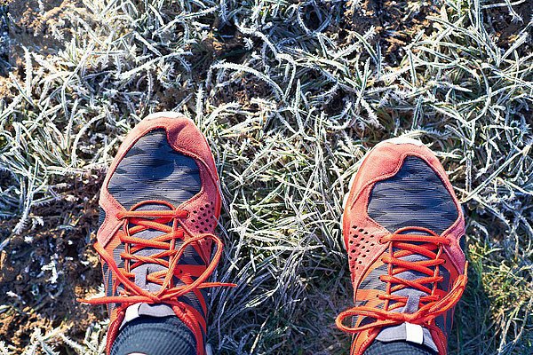 Overhead-Ansicht der Läuferfüße mit Laufschuhen auf frostigem Gras