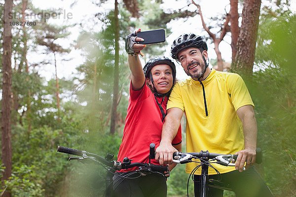 Glückliches Mountainbike-Pärchen posiert für Smartphone Selfie im Wald