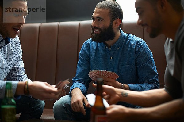 Drei junge erwachsene männliche Freunde beim Kartenspiel im traditionellen britischen Pub