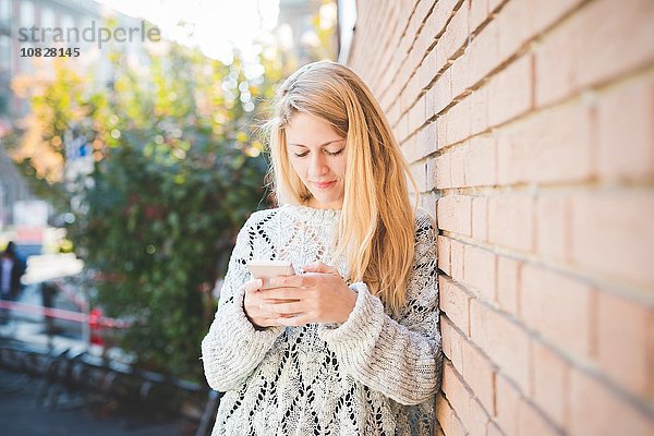Frau texten auf dem Smartphone  gegen die Ziegelwand