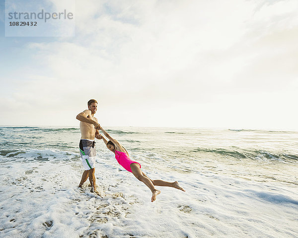 Kaukasischer Vater und Tochter spielen in den Wellen am Strand