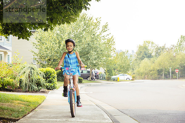 Gemischtrassiges Mädchen fährt Fahrrad auf dem Bürgersteig