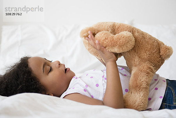 Gemischtrassiges Mädchen spielt mit Teddybär