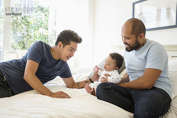 Schwule Väter spielen mit ihrem kleinen Sohn im Bett