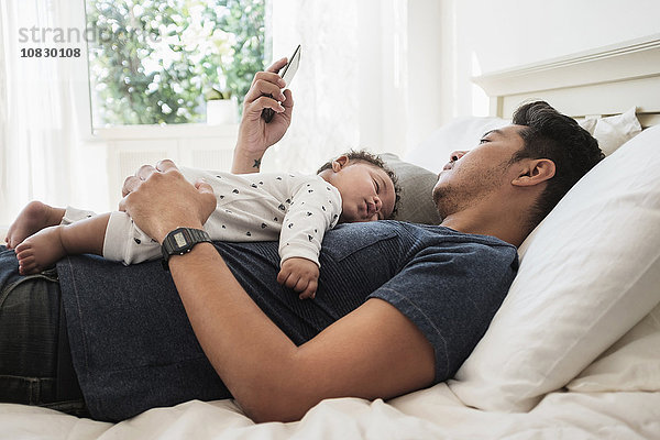 Vater benutzt Mobiltelefon mit schlafendem Babysohn