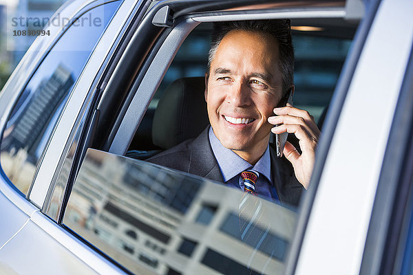 Gemischtrassiger Geschäftsmann  der im Auto mit seinem Handy telefoniert