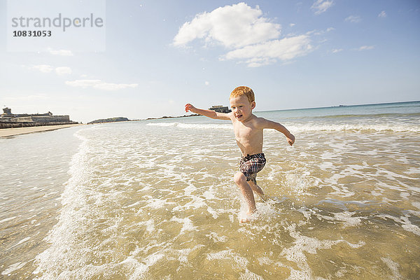 Kaukasischer Junge spielt in den Wellen am Strand