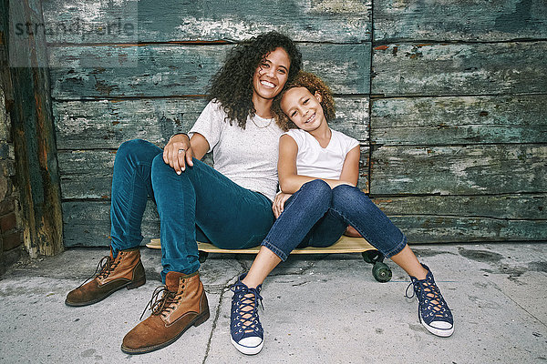 Gemischtrassige Mutter und Tochter sitzen auf einem Skateboard