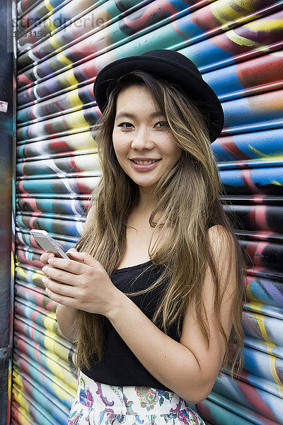 Asiatische Frau benutzt Mobiltelefon in der Nähe einer Graffiti-Wand