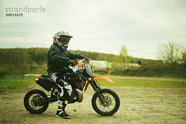 Kaukasischer Mann fährt Dirt Bike auf einem Feld