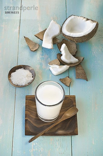 Ein Glas Kokosmilch  aufgeschlagene Kokosnuss und Kokosraspeln