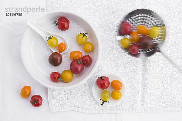 Verschiedenfarbige Tomaten in Porzellanschale & auf Sieblöffel