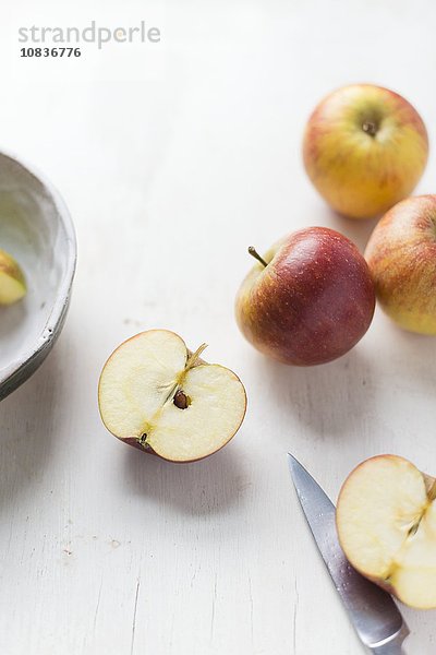 Äpfel auf weissem Untergrund mit halbiertem Apfel und Messer