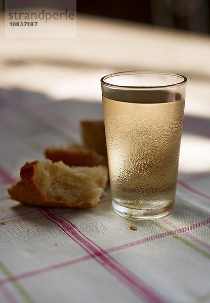 Weissweinglas und Brot auf sonnigem Tisch