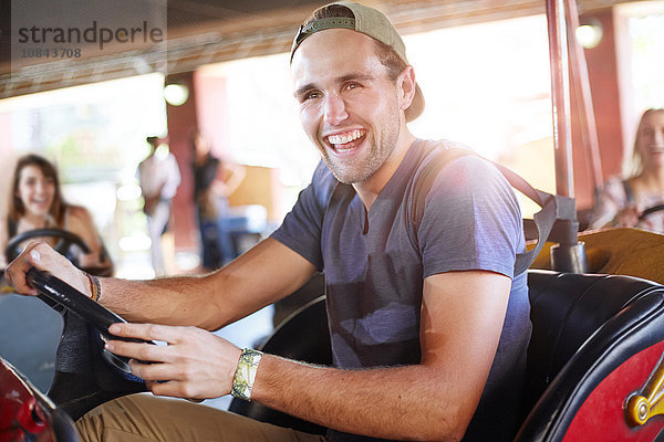 Lachender junger Mann auf Autoscooter im Vergnügungspark