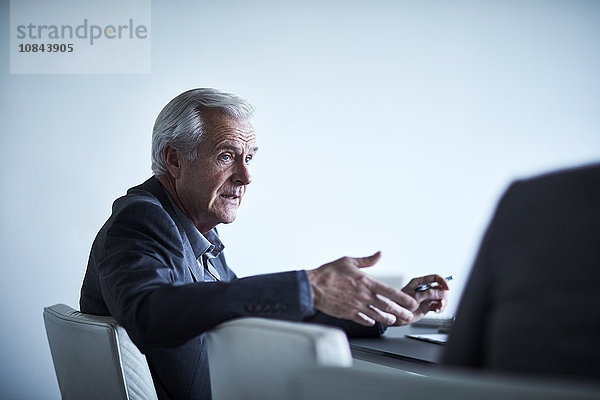 Senior Geschäftsmann gestikuliert und redet im Meeting