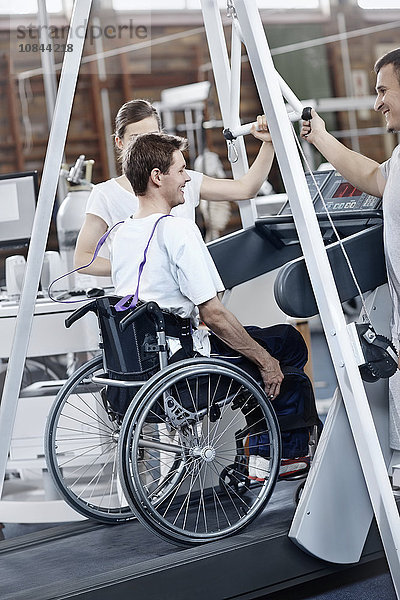 Physiotherapeuten führen Mann im Rollstuhl auf dem Laufband