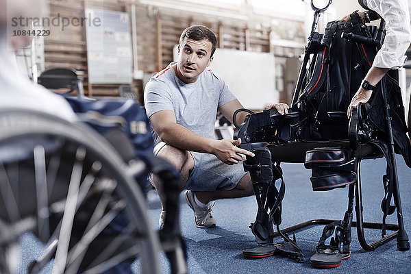 Physiotherapeutin  die dem Menschen im Rollstuhl die Ausrüstung erklärt