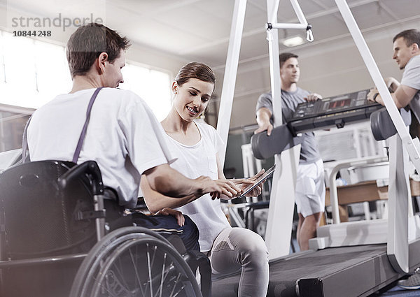 Physiotherapeutin zeigt dem Menschen im Rollstuhl Tablet PC